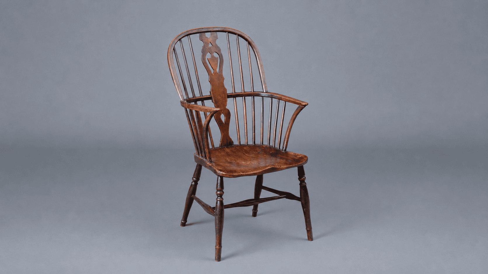 A Windsor chair with splayed legs socketed into a solid seat, spindles and splat rising from above